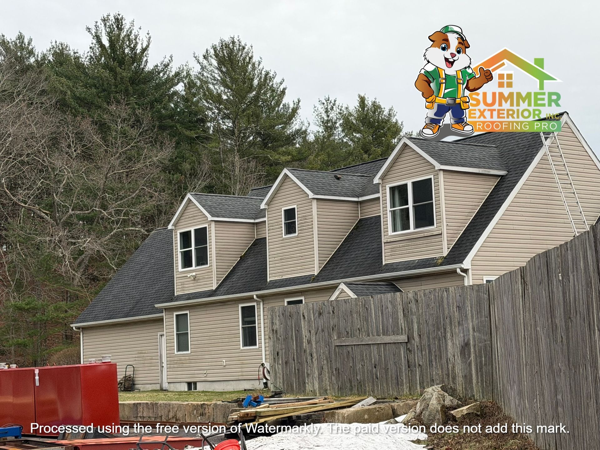 Exterior of a two-story tan house with a dark roof and dormer windows, featuring a cartoon mascot logo on the roof.