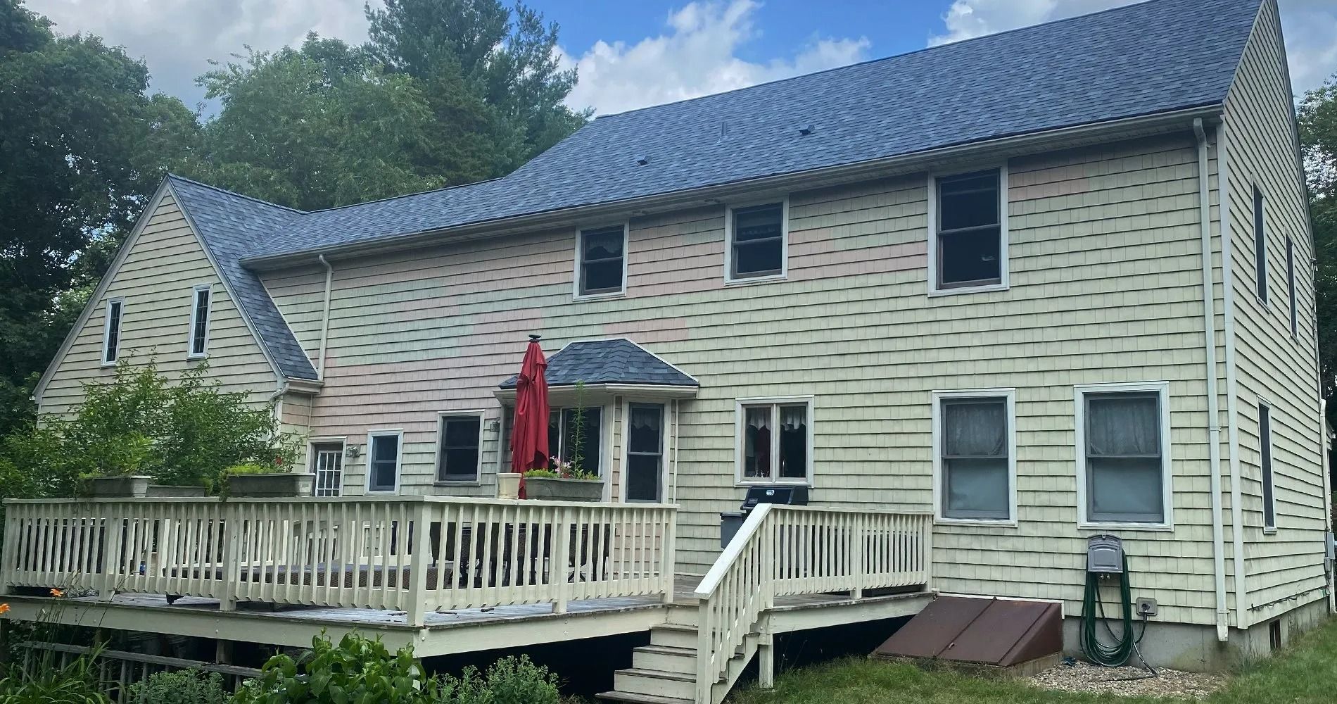 Two-story house with light siding and a deck. The roof is blue. A red umbrella provides shade.