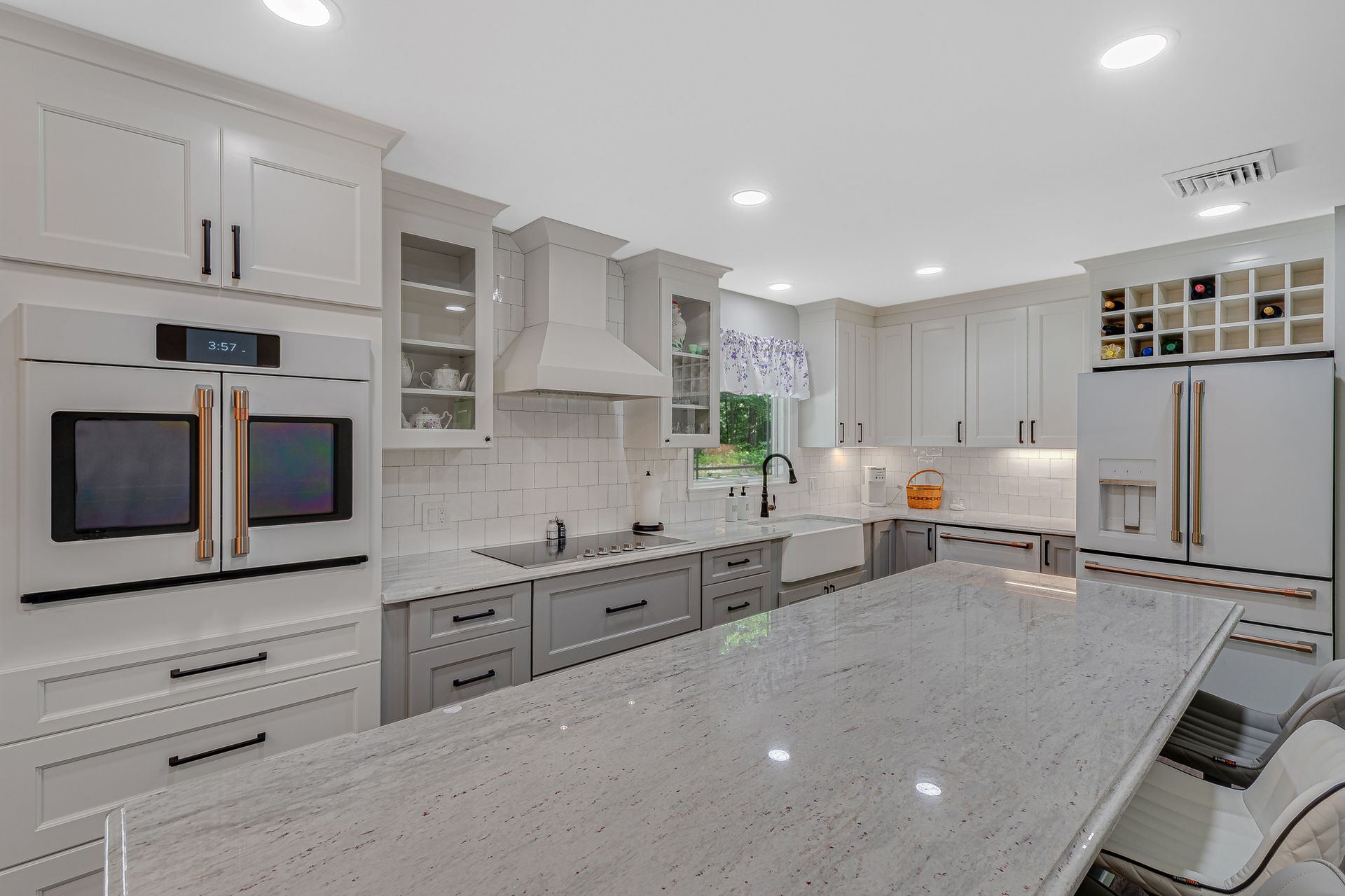 A kitchen with white cabinets, granite counter tops, kitchen appliances and a large island