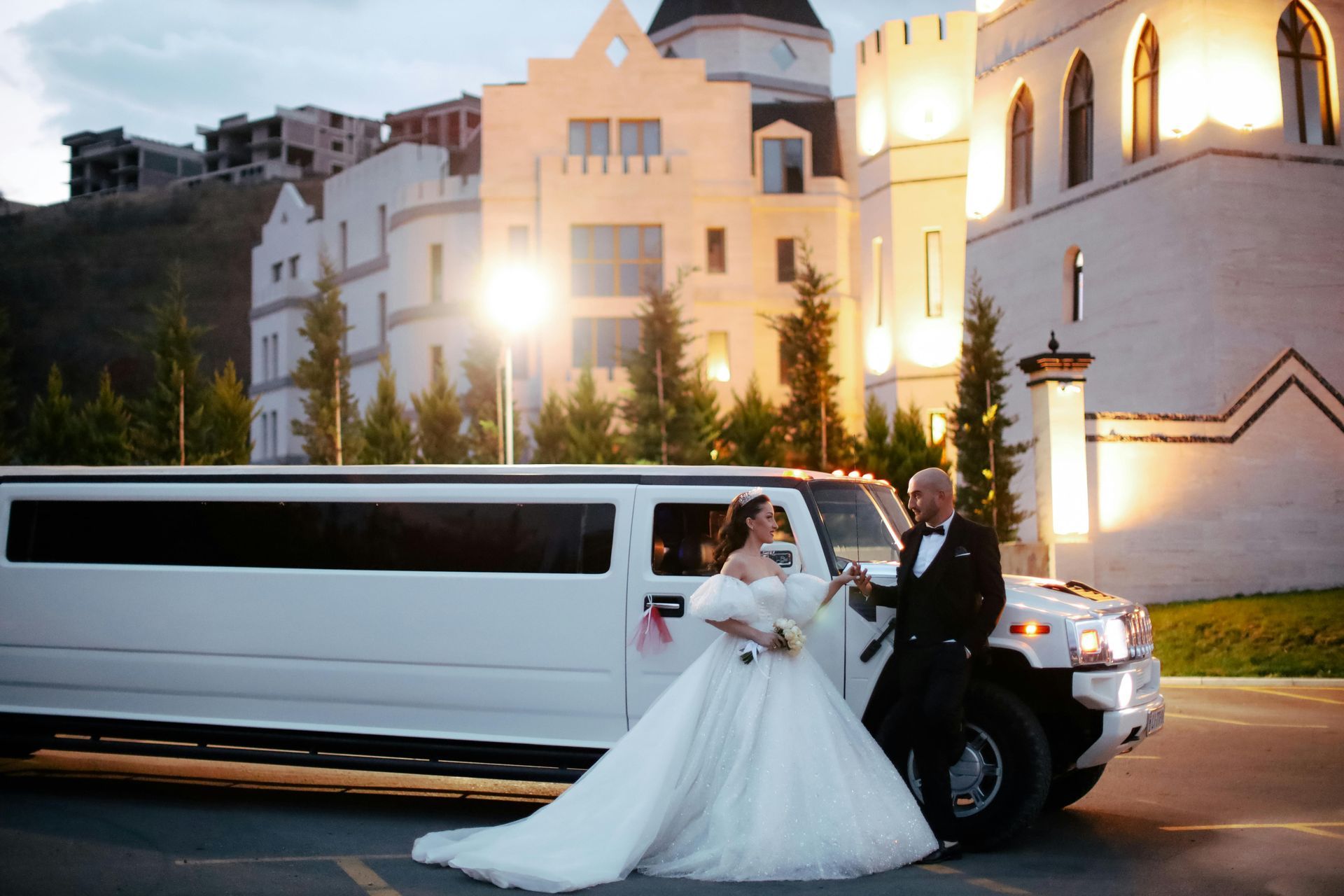 Newlyweds smiling beside white Hummer limo at wedding venue – stylish, reliable limo service near me