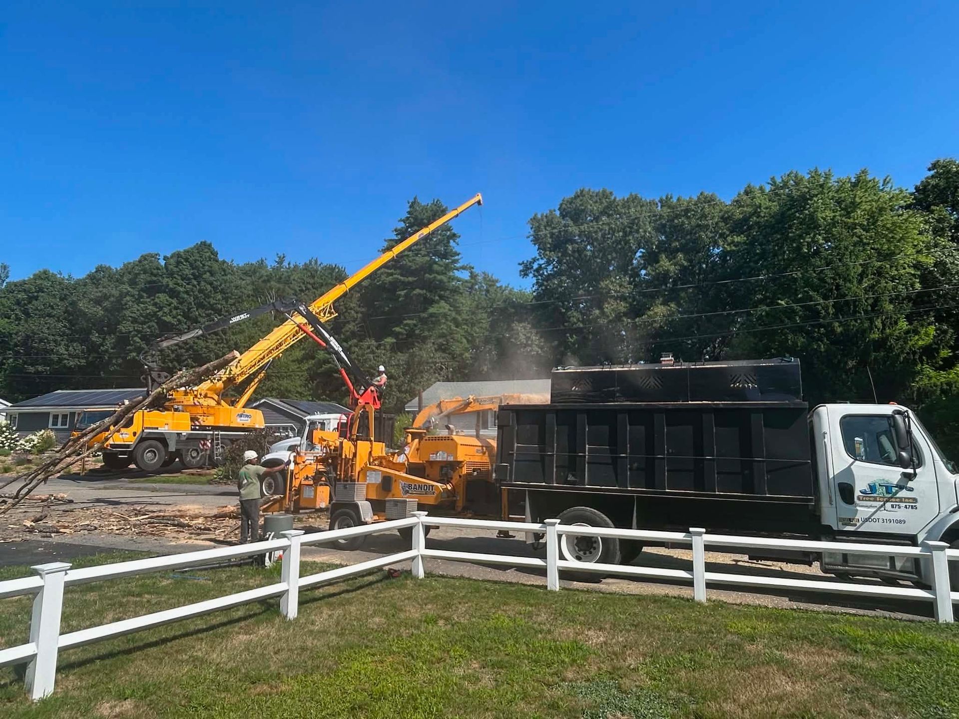 Construction crew using a yellow crane to load debris into a black dump truck on a sunny site