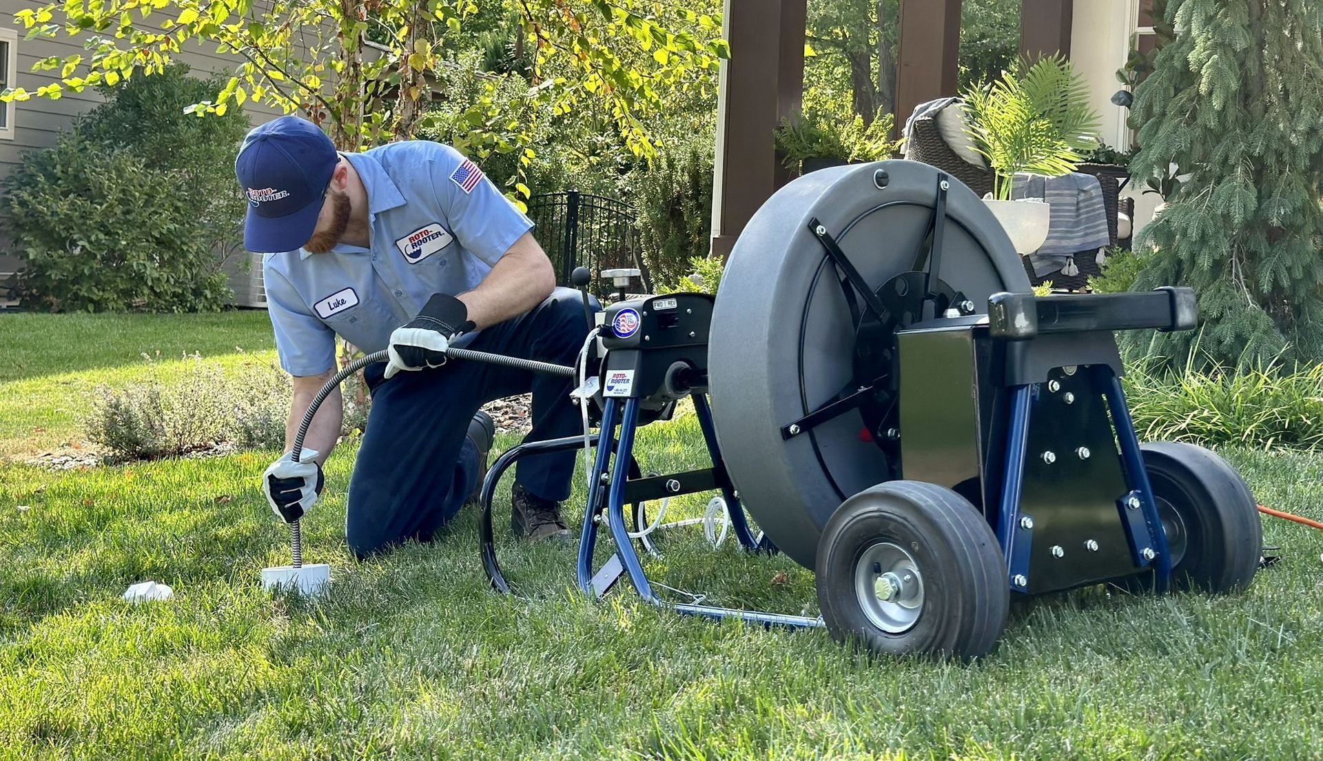 Plumber of Roto-Rooter working on a drain, van parked in front of a house.