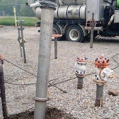 Pipes and valves in a gravel lot with a tanker truck in the background.