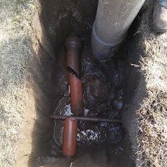 Broken orange pipe in a trench with standing water and a gray pipe above.