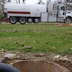 Septic truck emptying a septic tank in a grassy field.