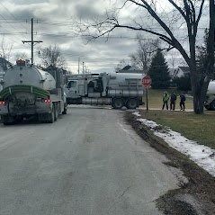Two tanker trucks parked on a street with workers standing nearby. Cloudy day.
