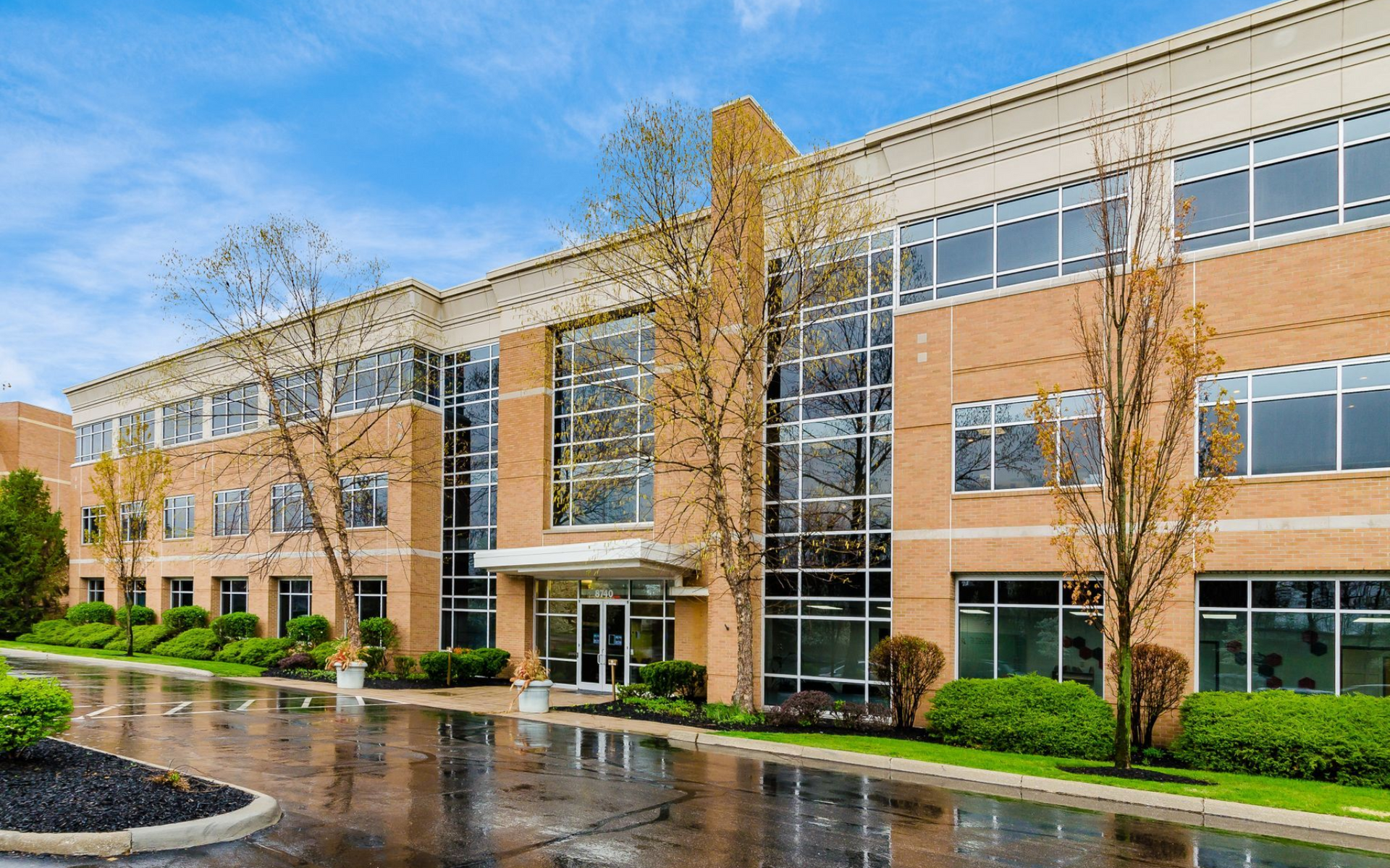 Office building with brick and glass facade, trees and blue sky.