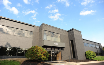 Gray office building with glass entryway under a blue sky.