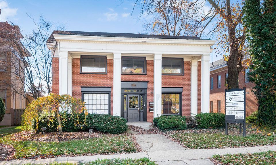 Brick building with white columns, windows, and a small sign on a grassy lawn.