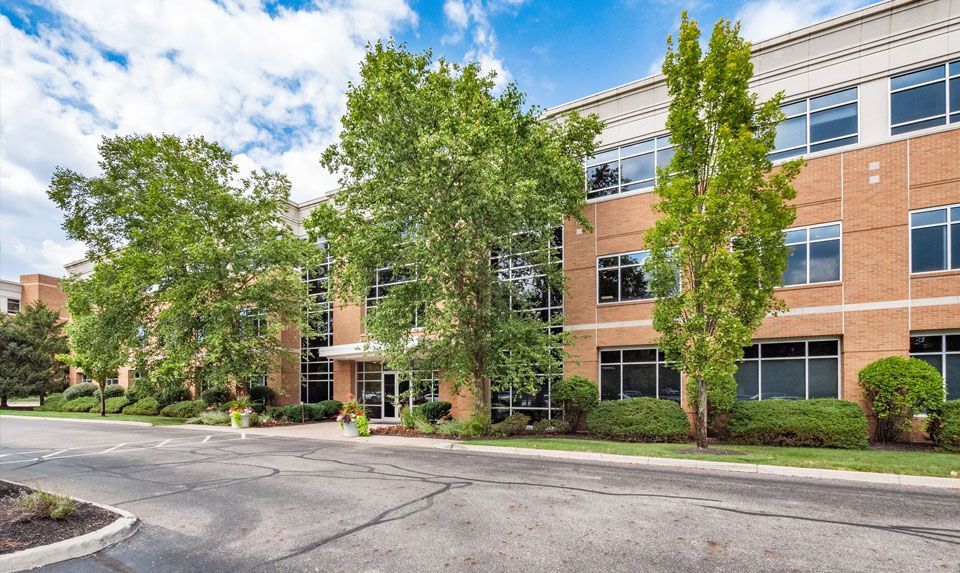 Office building with brick and glass facade, trees and blue sky.
