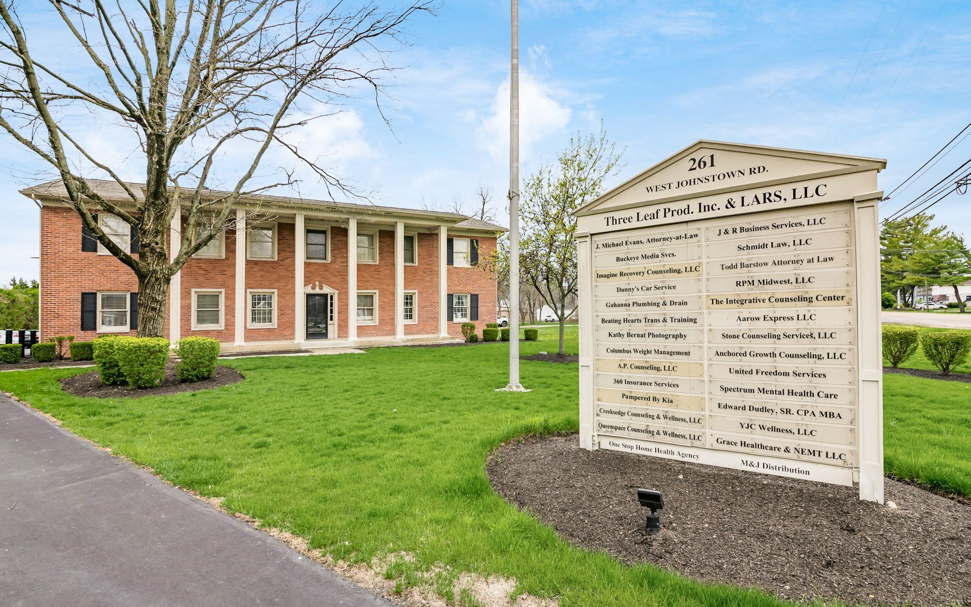 Brick building with columns and sign listing tenants on a green lawn.
