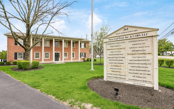 Brick building with columns and sign listing tenants on a green lawn.