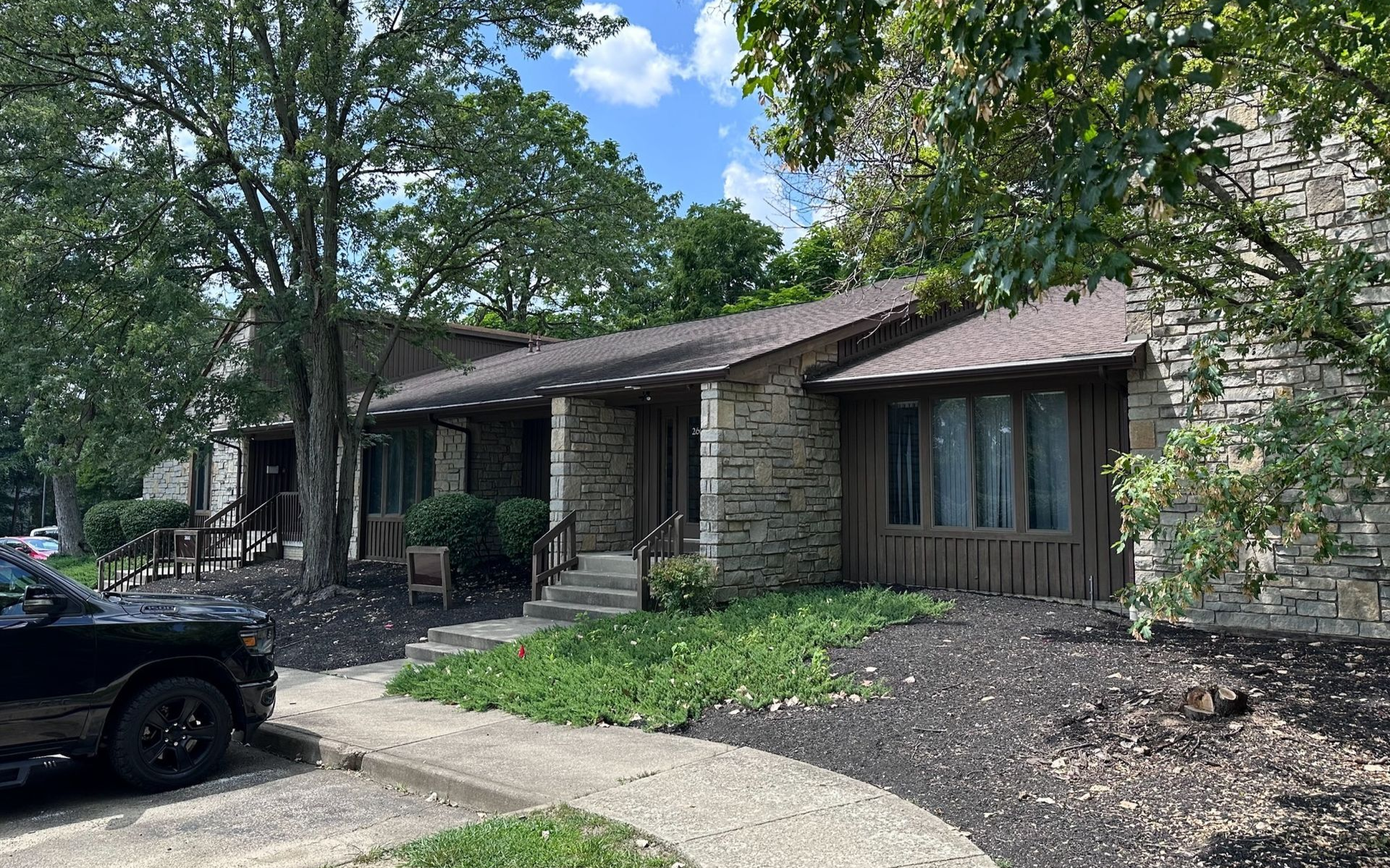 Exterior view of a stone and wood house with a dark car parked in front.
