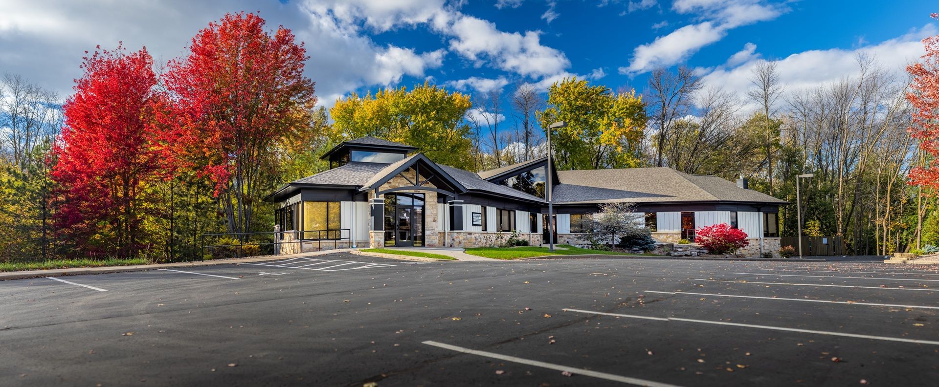 Modern building with autumn trees beside an empty parking lot under a blue sky