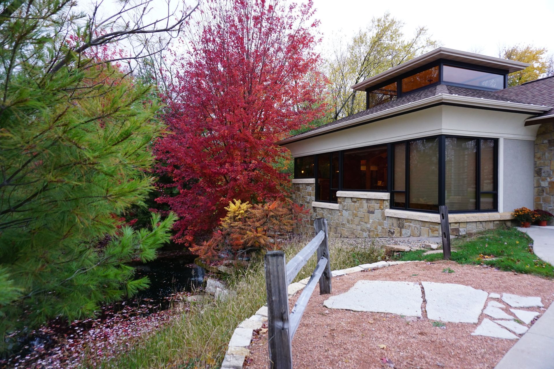 Modern house with stone facade, red autumn tree, and landscaped garden path