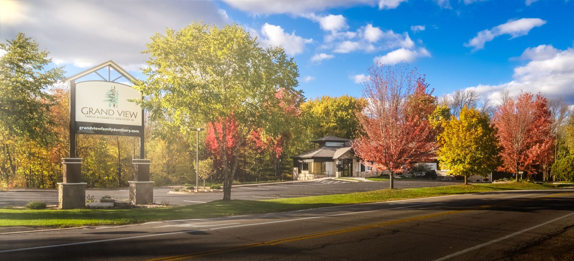 Autumn entrance sign and building under colorful fall trees beside a road