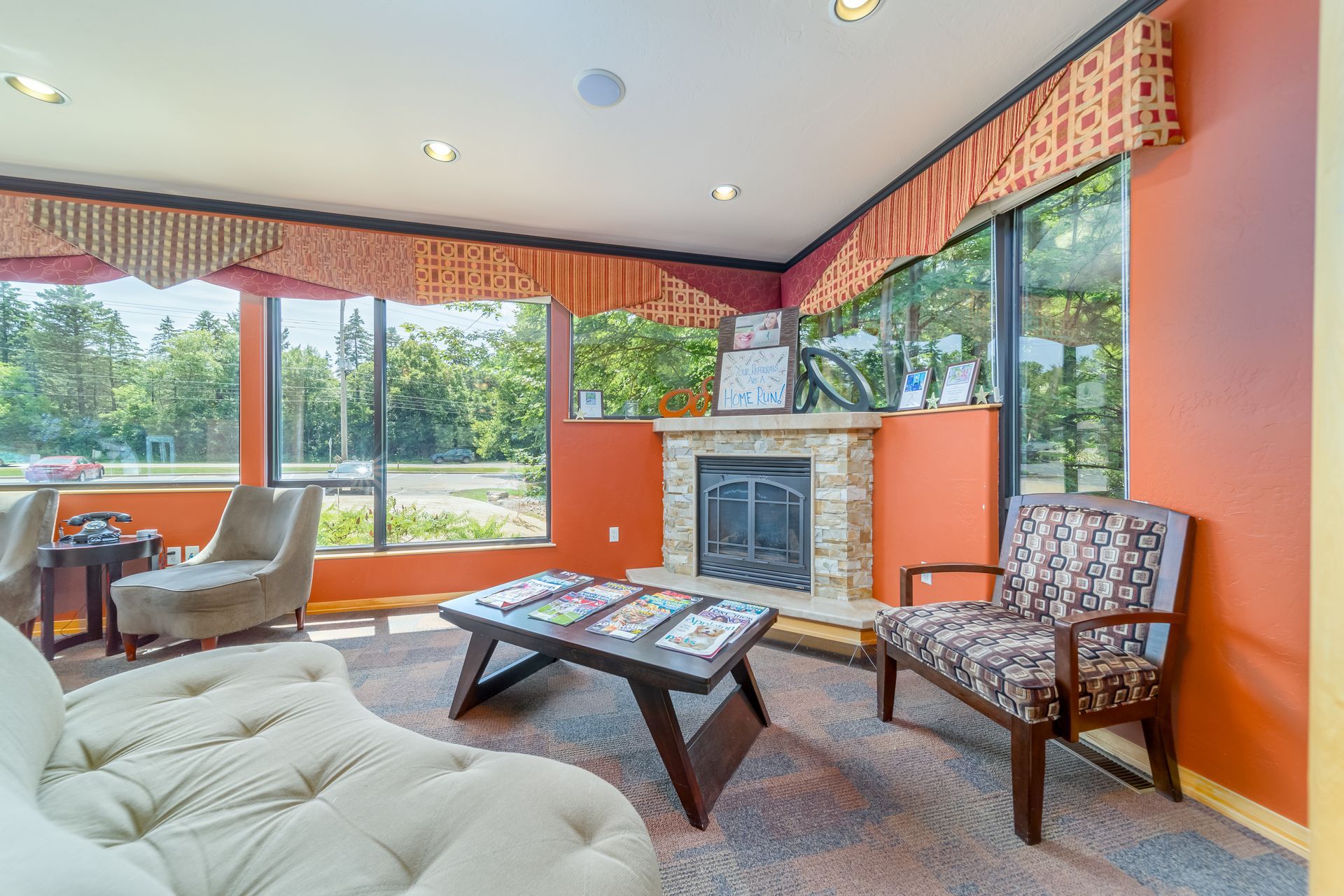 Bright sunroom with orange walls, large windows, fireplace, and cozy seating around a coffee table