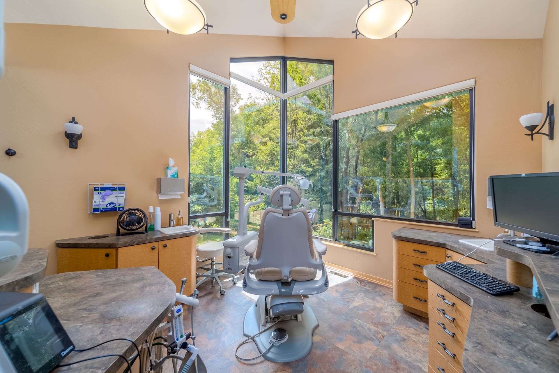 Dental exam room with chair, tools, monitors, and large windows overlooking trees