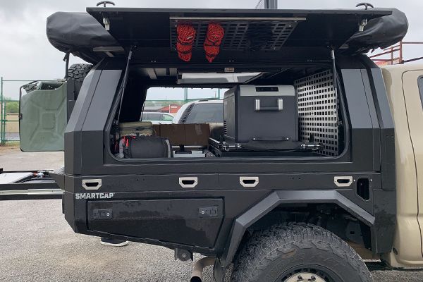 The back of a camper with the canopy open and a cooler in the back.