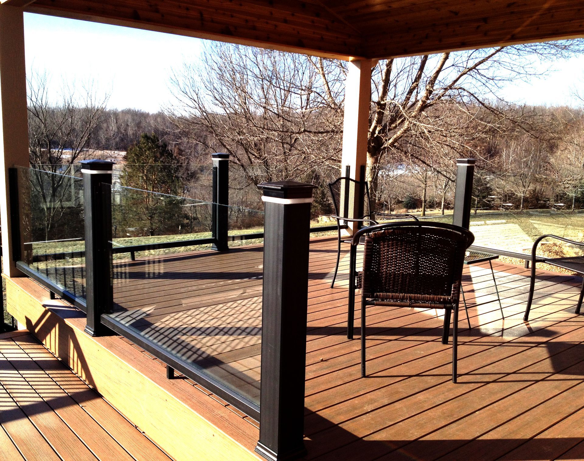 A wooden deck with a black railing and chairs