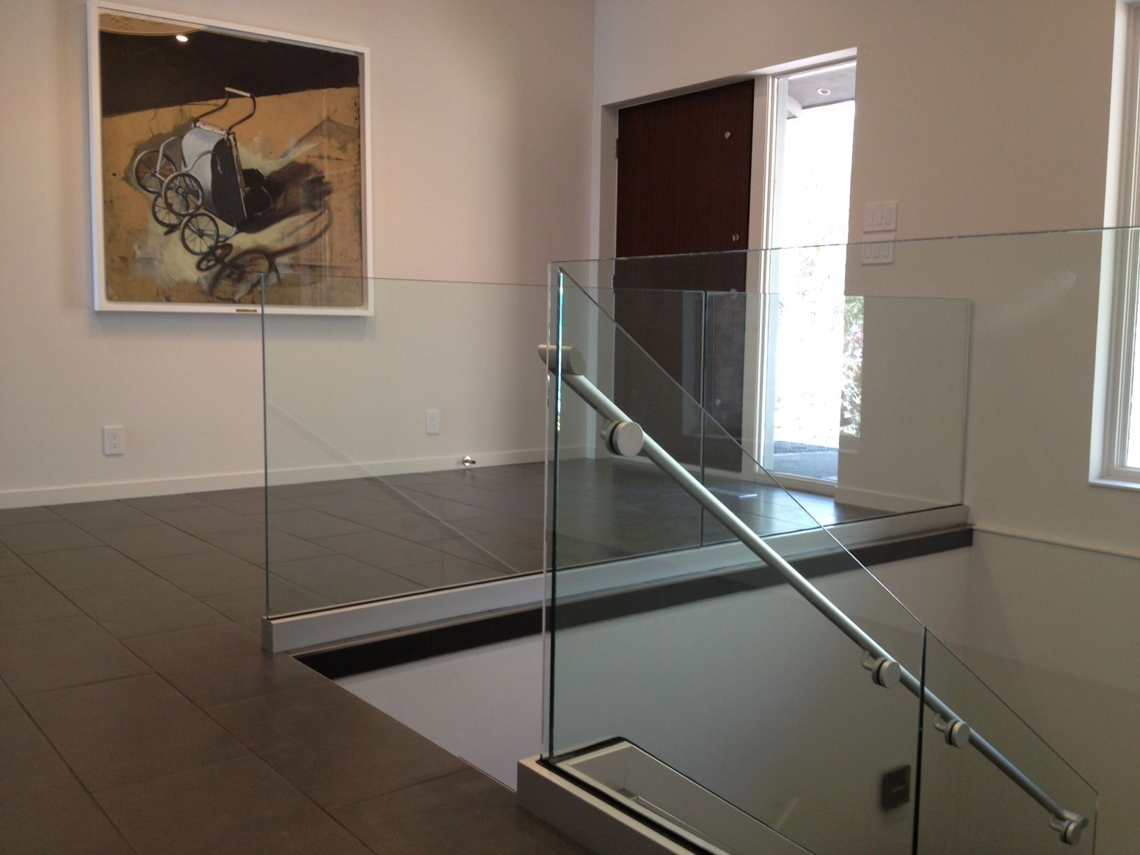 A staircase with a glass railing and a painting on the wall above it