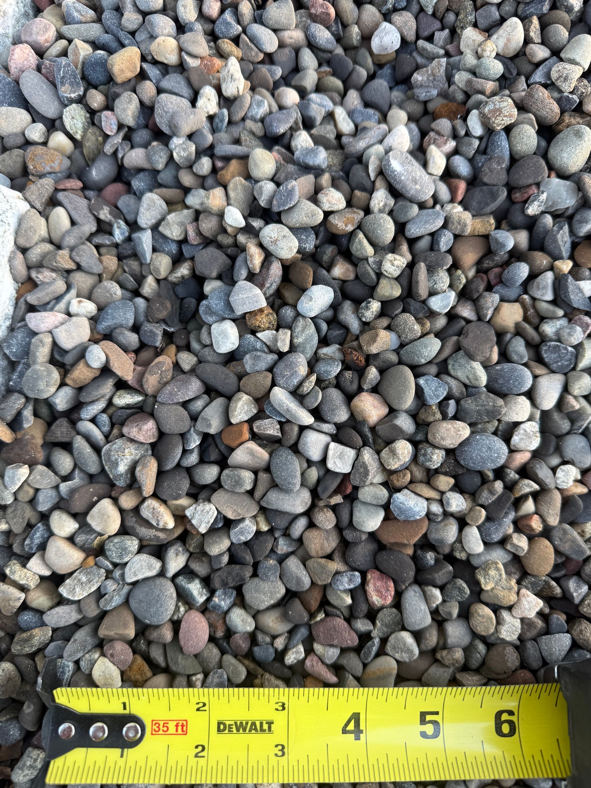 Close-up of small gray and brown pebbles with a yellow measuring tape along the bottom edge