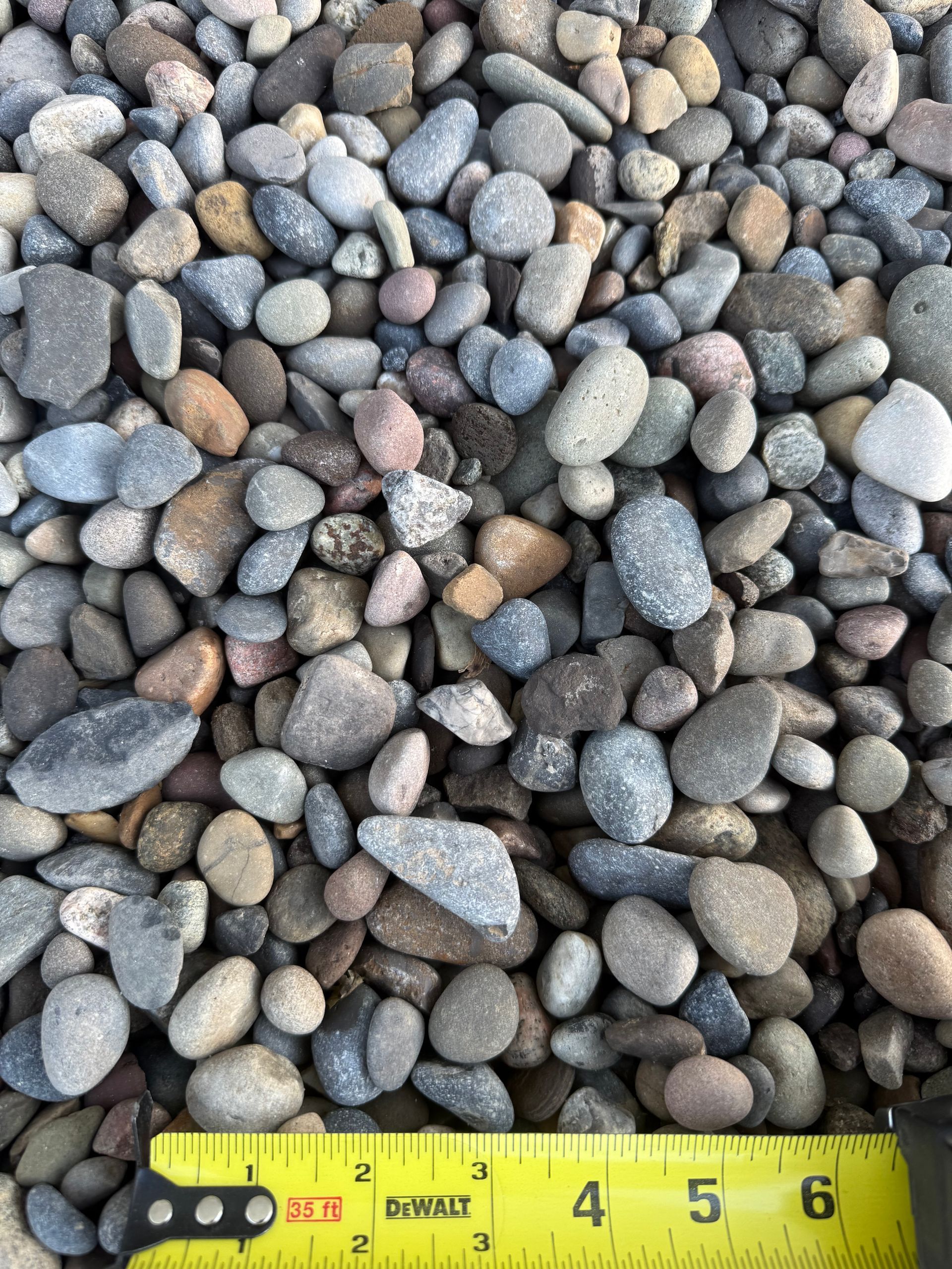Close-up of mixed gray pebbles with a yellow measuring tape along the bottom edge.