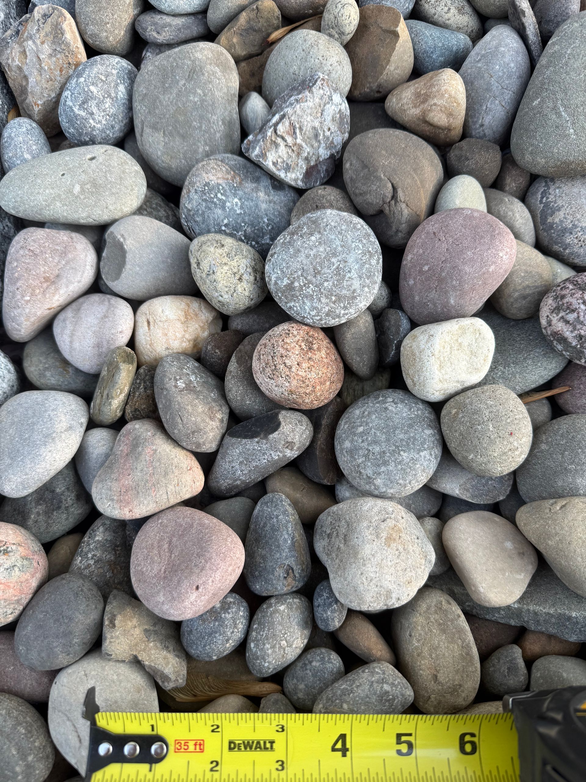 Assorted round pebbles with a yellow measuring tape along the bottom edge