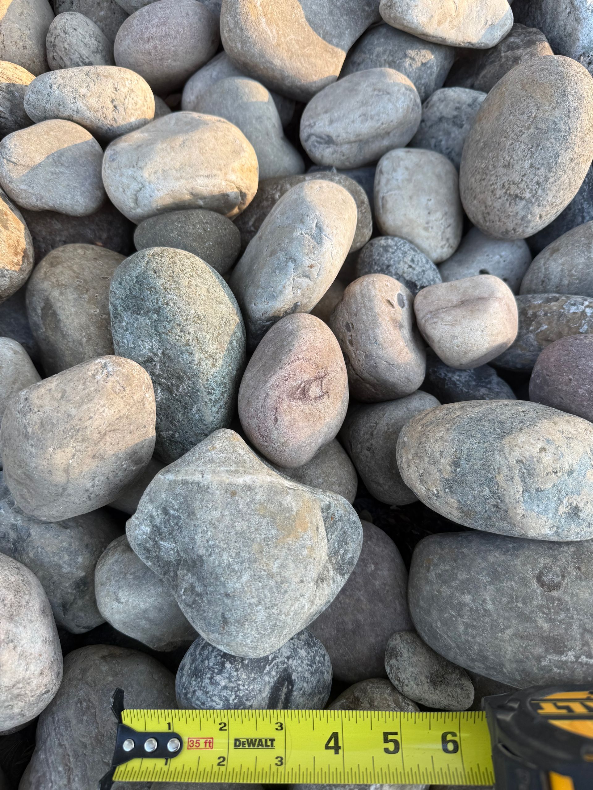 Gray river pebbles piled together with a yellow measuring tape along the bottom edge