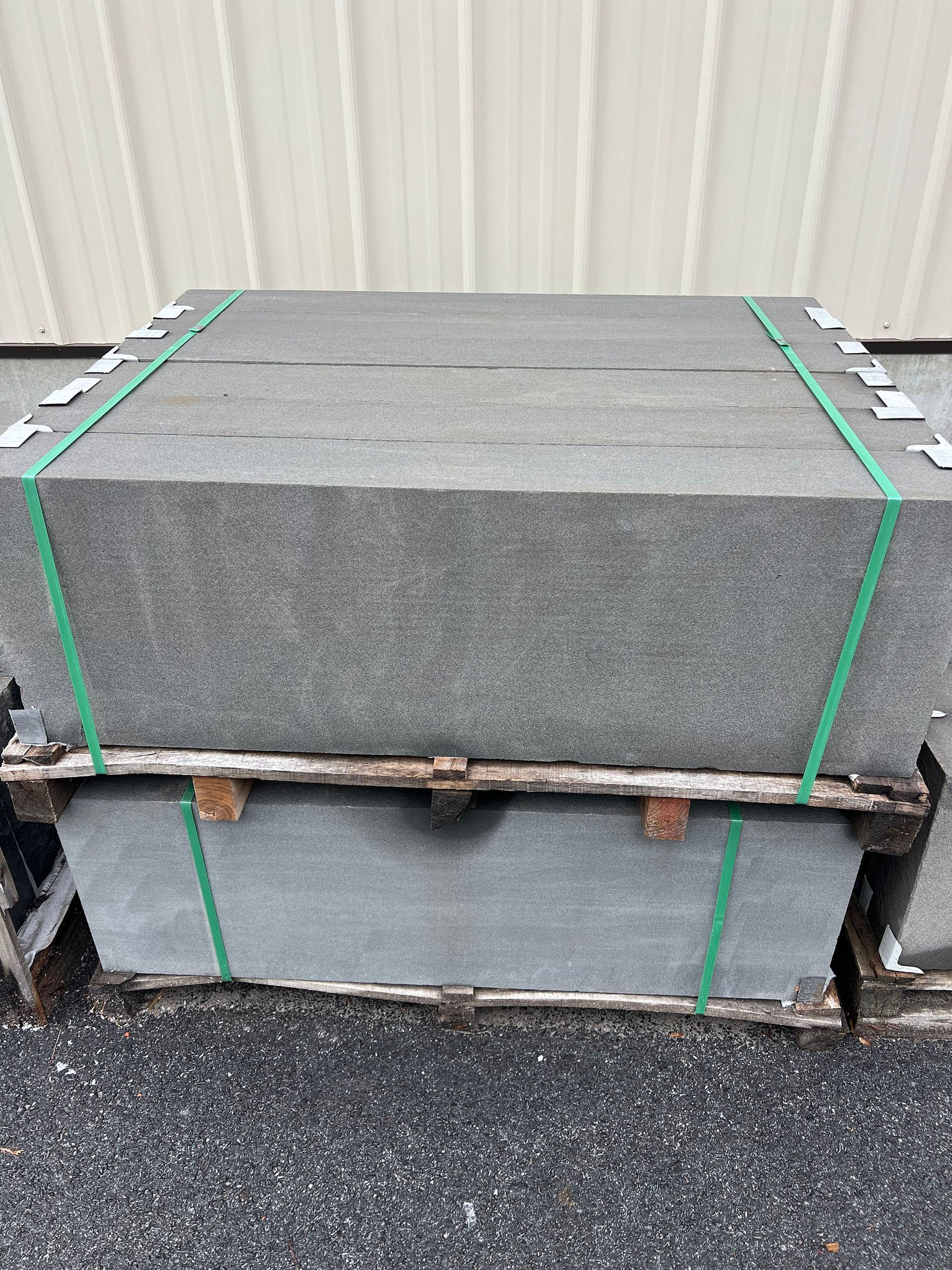 A pallet of concrete blocks with green straps is stacked on top of each other.