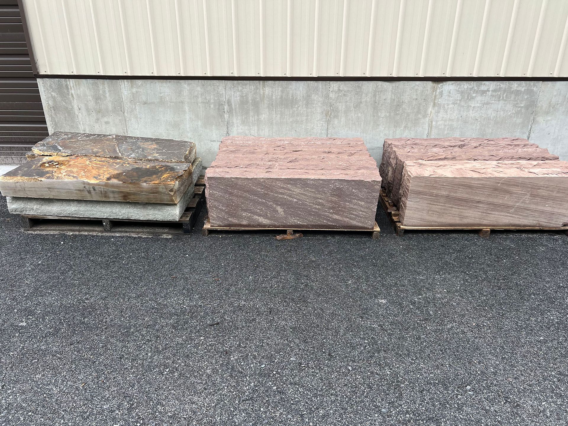 Three pallets of rocks are sitting on the ground in front of a building.