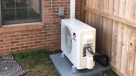 Three air conditioners are sitting outside of a house.