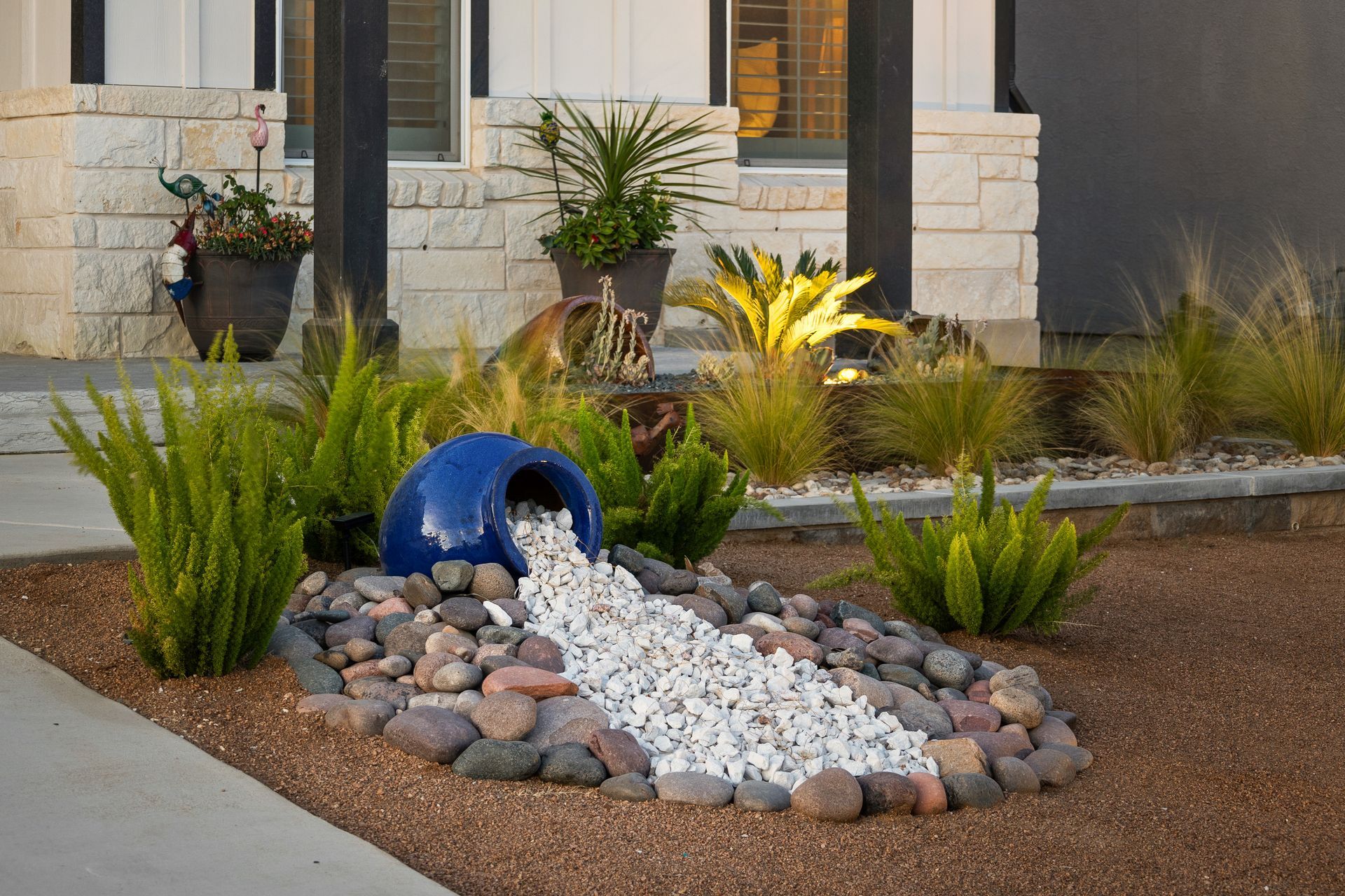 A blue vase is pouring white rocks into a garden.