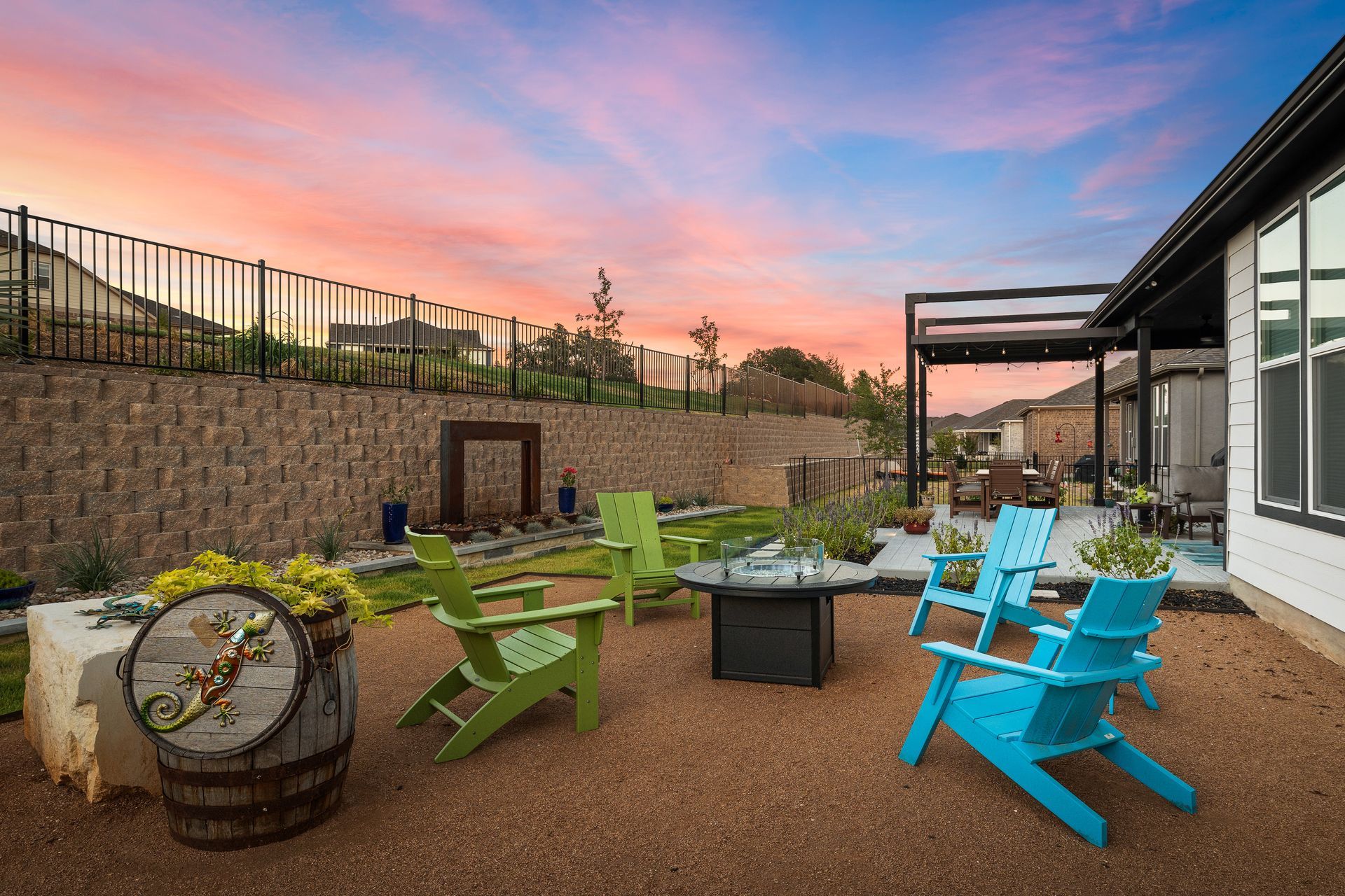A patio with chairs and a fire pit in front of a house at sunset.