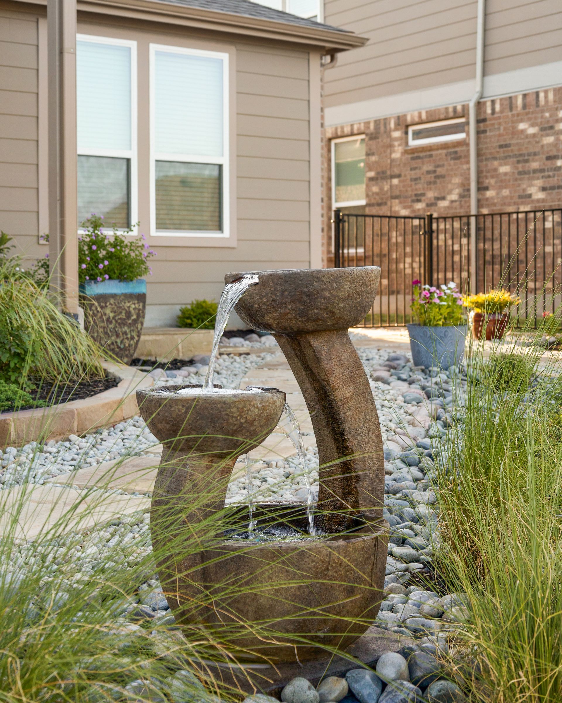 A fountain is in the middle of a garden in front of a house.