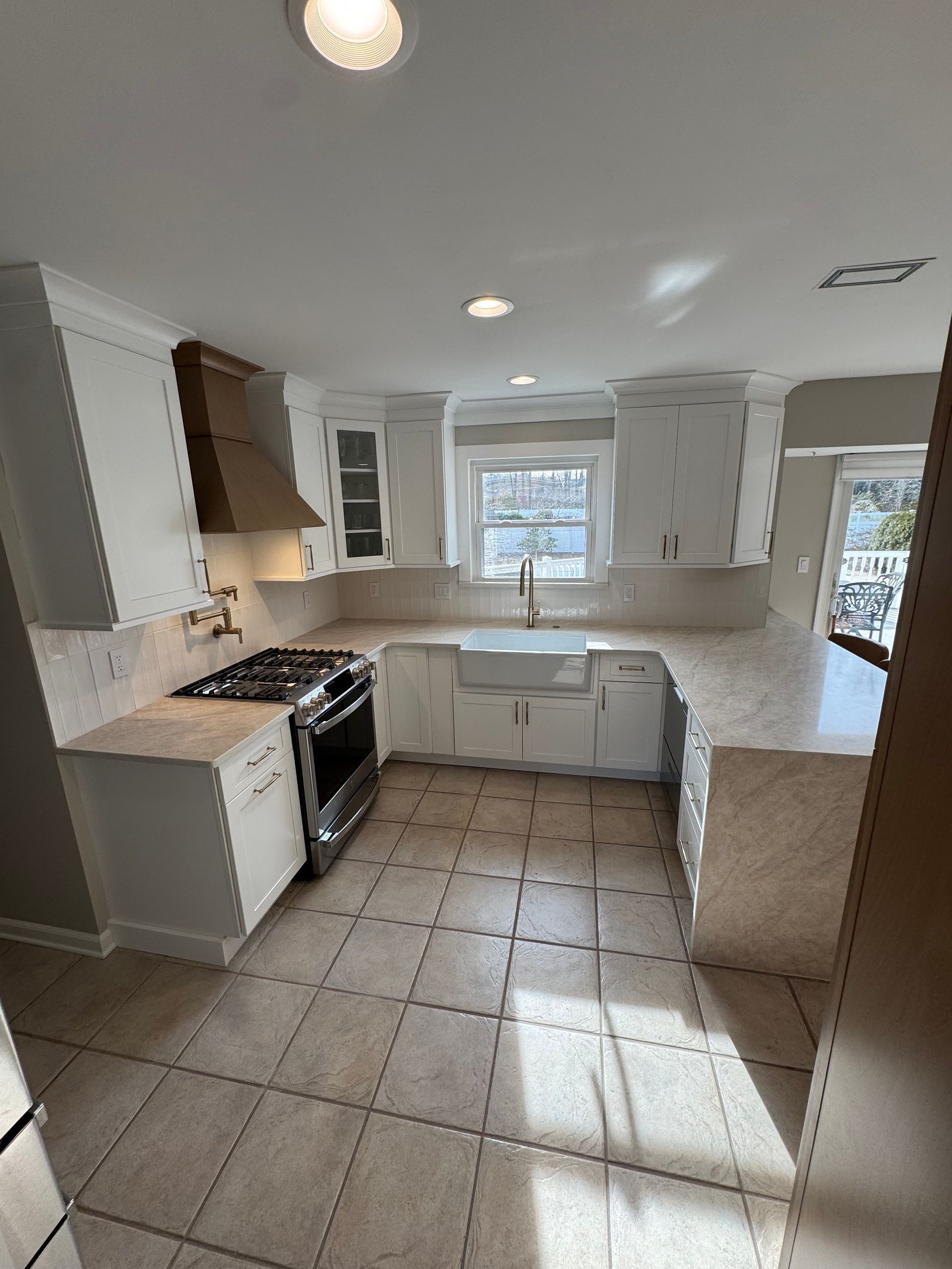 U-shaped white kitchen with beige countertops and tile floor, stainless steel appliances, and a window above the sink.