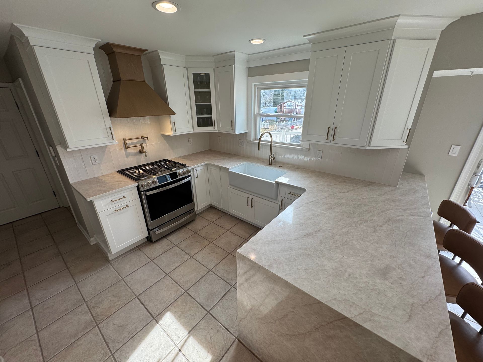 White kitchen with stainless steel appliances, marble countertops, and beige tiled floors.