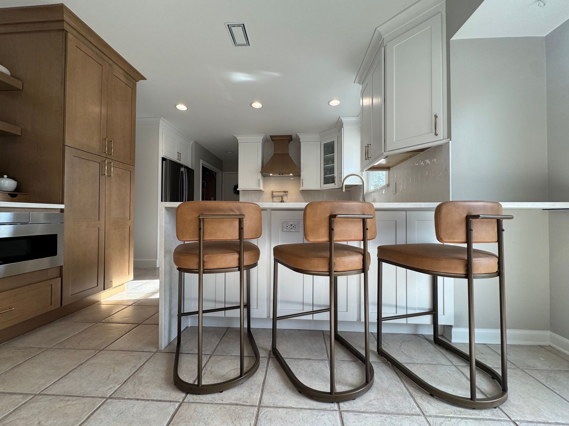 Kitchen with three brown leather bar stools at white island.