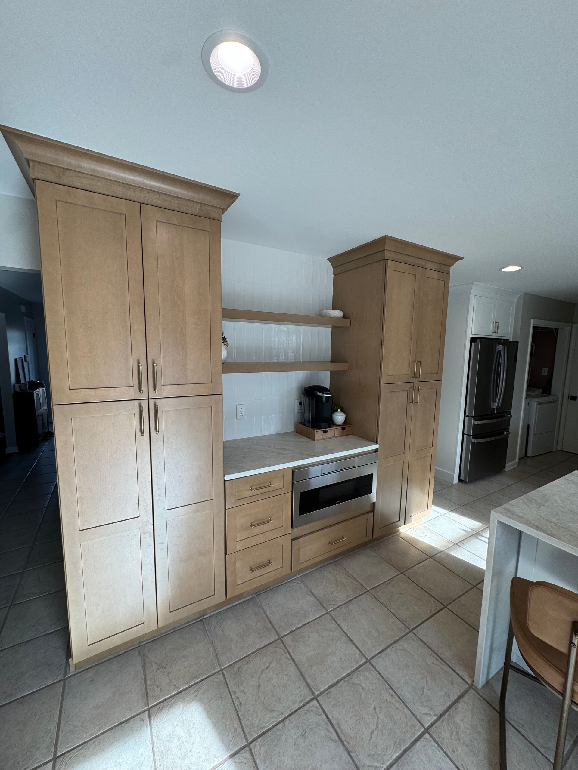 Kitchen cabinets in light wood tone with built-in microwave, open shelves, and tan tile floor.