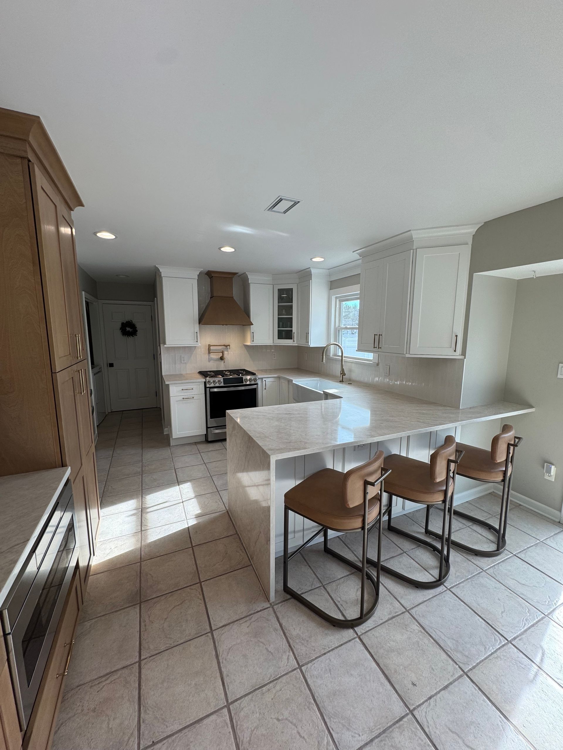 Modern kitchen with white cabinets, island with stools, and tile flooring.