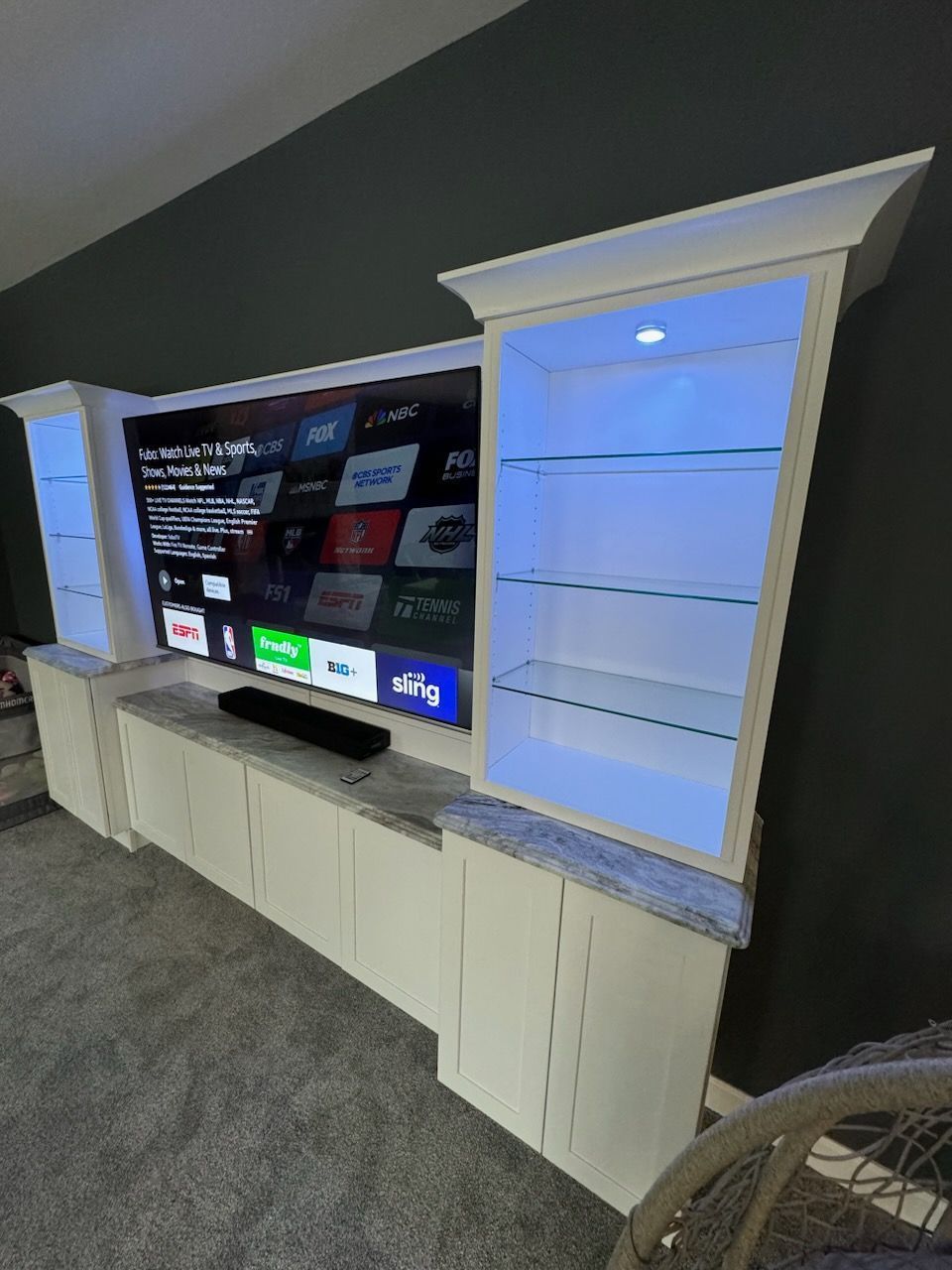 White entertainment center with TV, shelves, and gray countertop. Blue lights illuminate the cabinet.