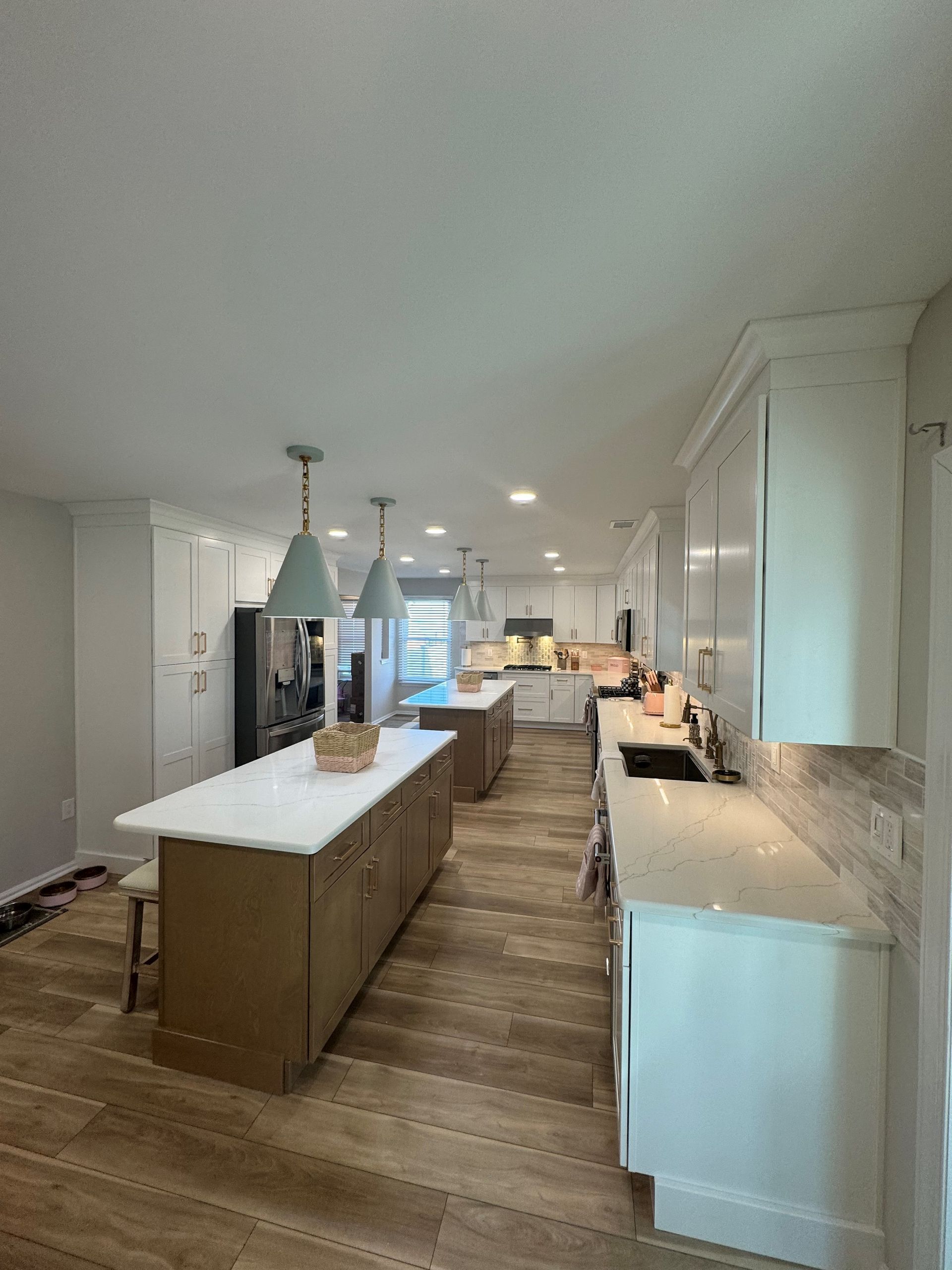 Spacious modern kitchen with two islands, light wood floor, white cabinetry, and gray pendant lights.