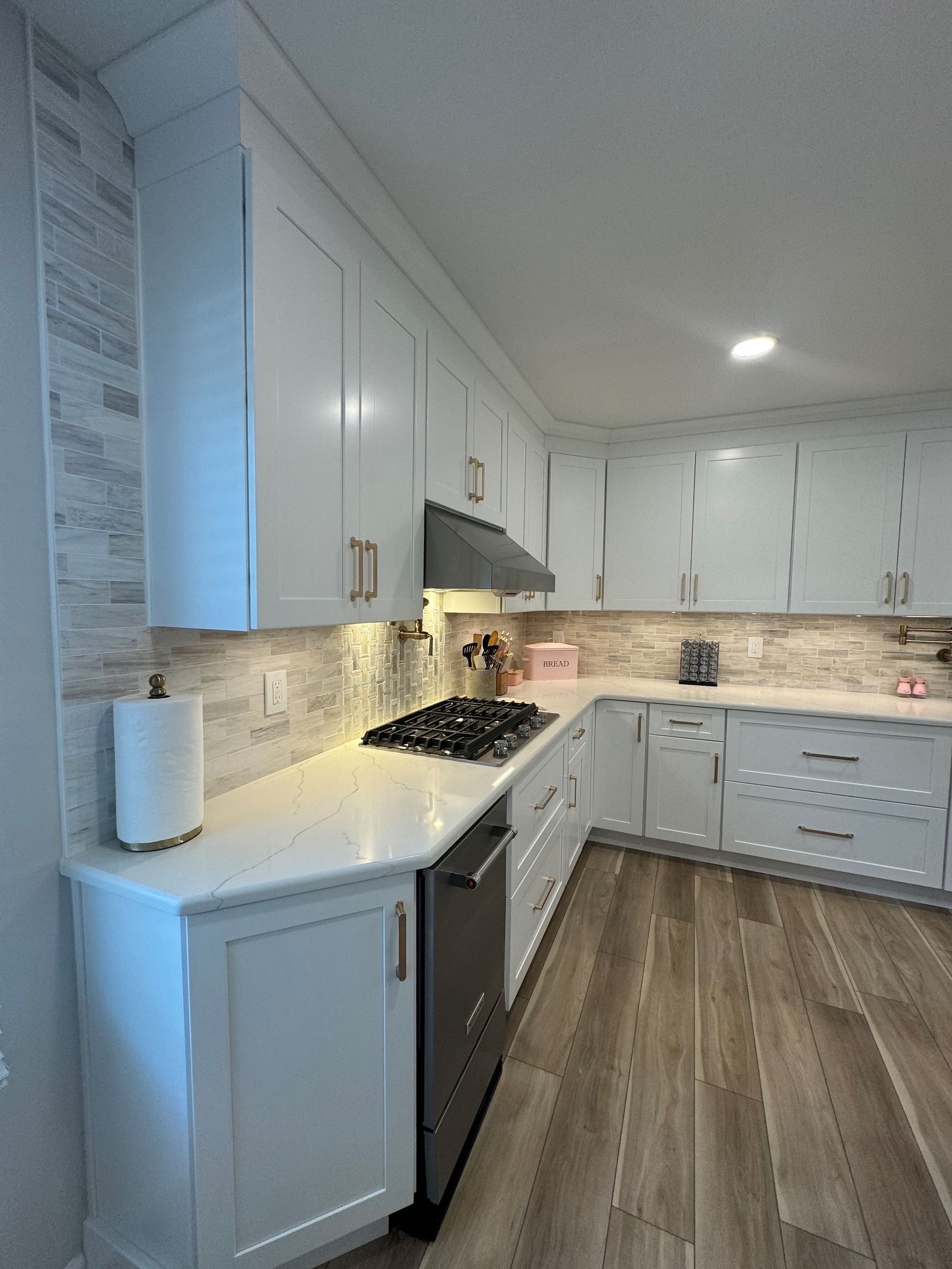 White kitchen with light wood floor, white cabinets, stainless steel appliances, and tiled backsplash.
