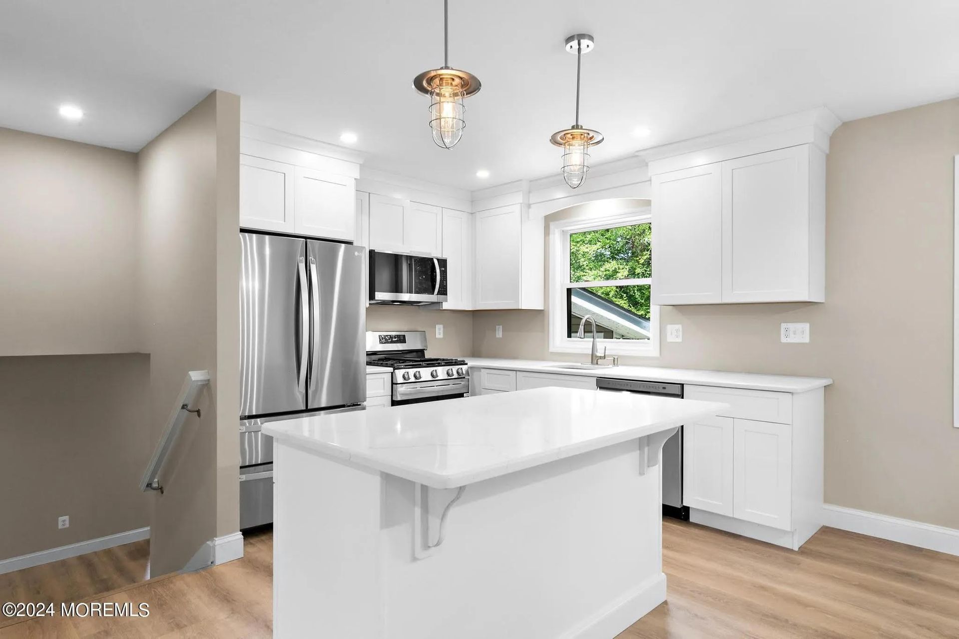 White kitchen with stainless steel appliances, white cabinets, island, and light wood floors.