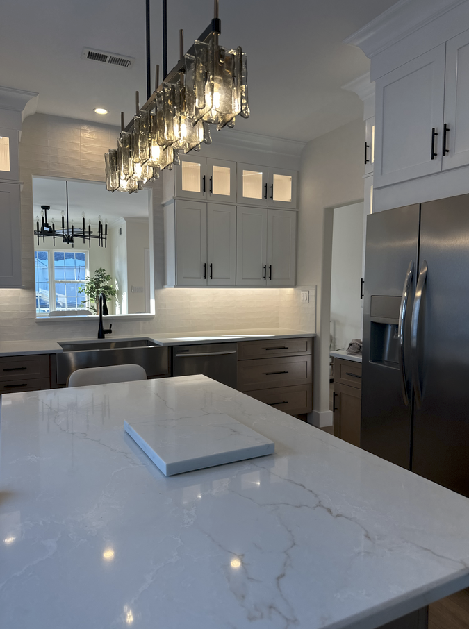 Modern kitchen with large island, stainless steel refrigerator, and decorative light fixtures.