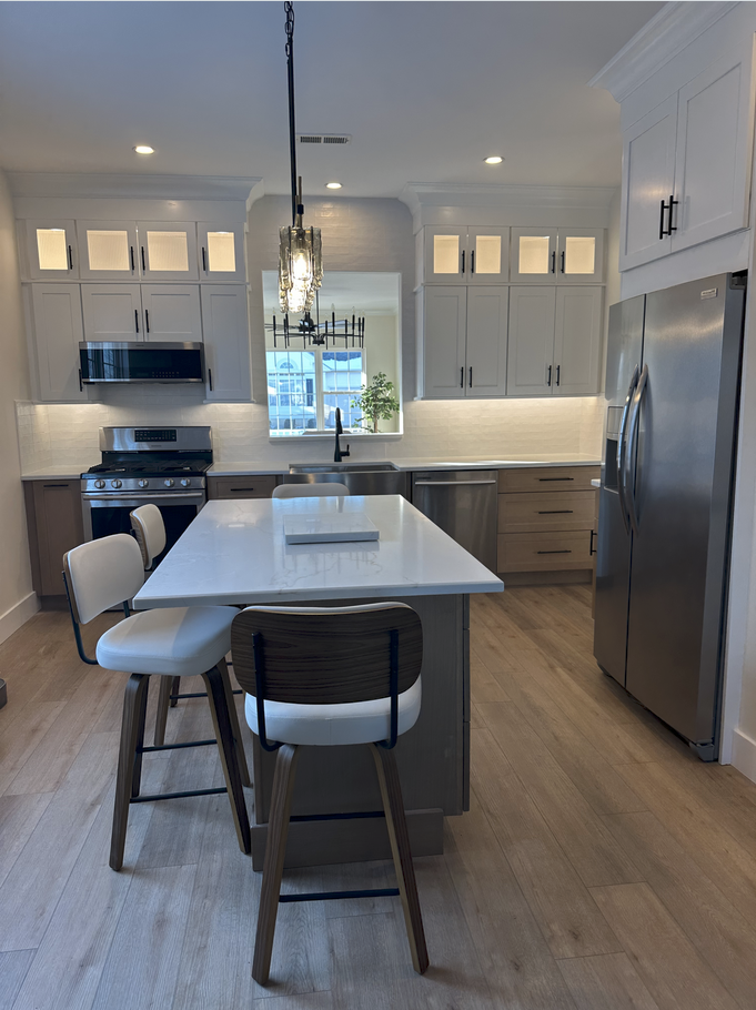 Modern kitchen with white cabinets, island, stainless steel appliances, and two bar stools.
