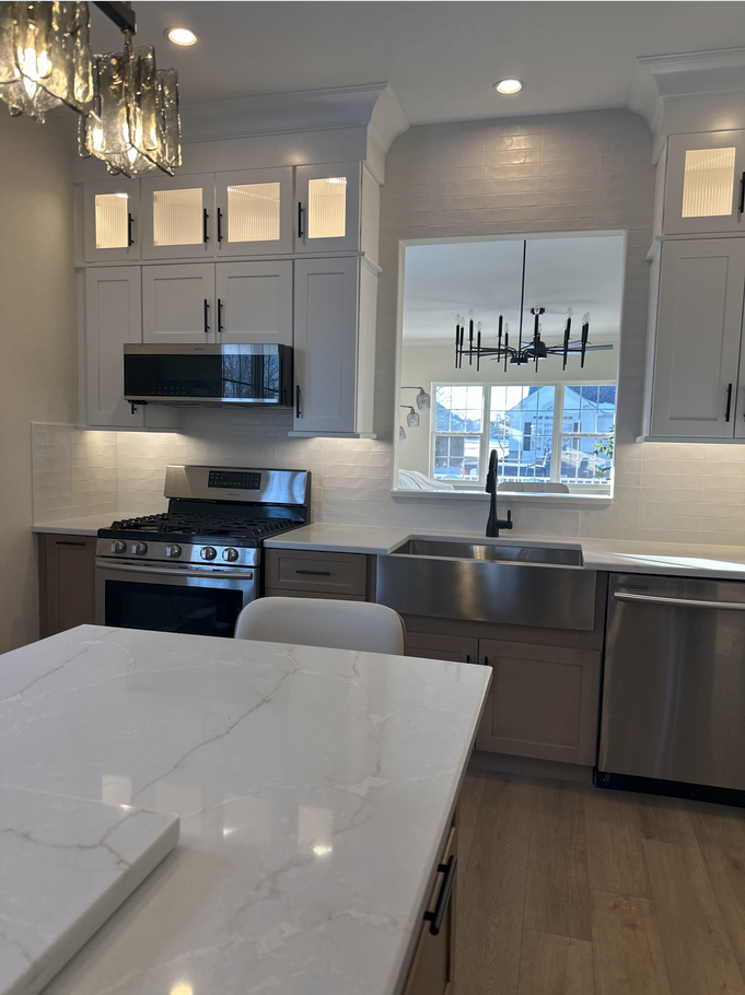 Modern kitchen with white and gray cabinets, stainless steel appliances, and a marble island.