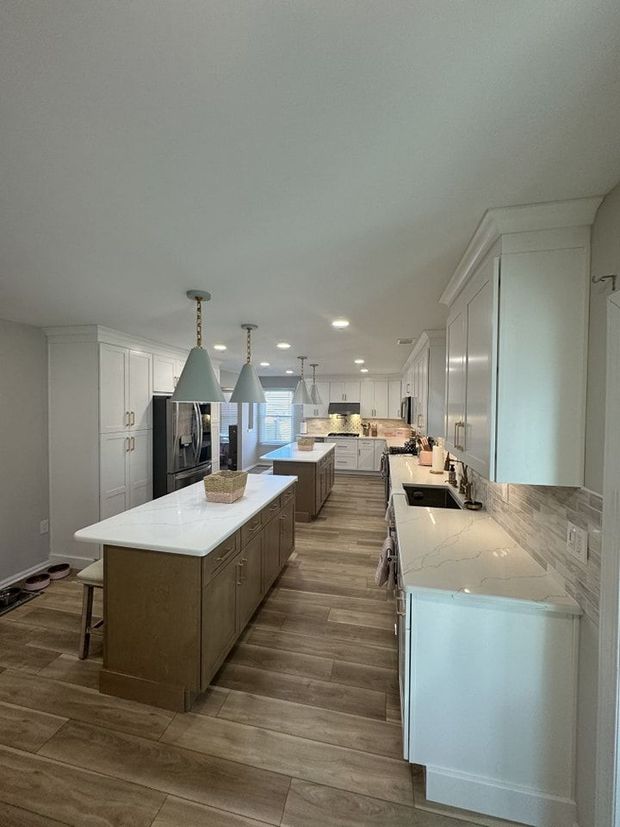 Spacious kitchen with wood floors, two islands, white cabinets, and pendant lights.