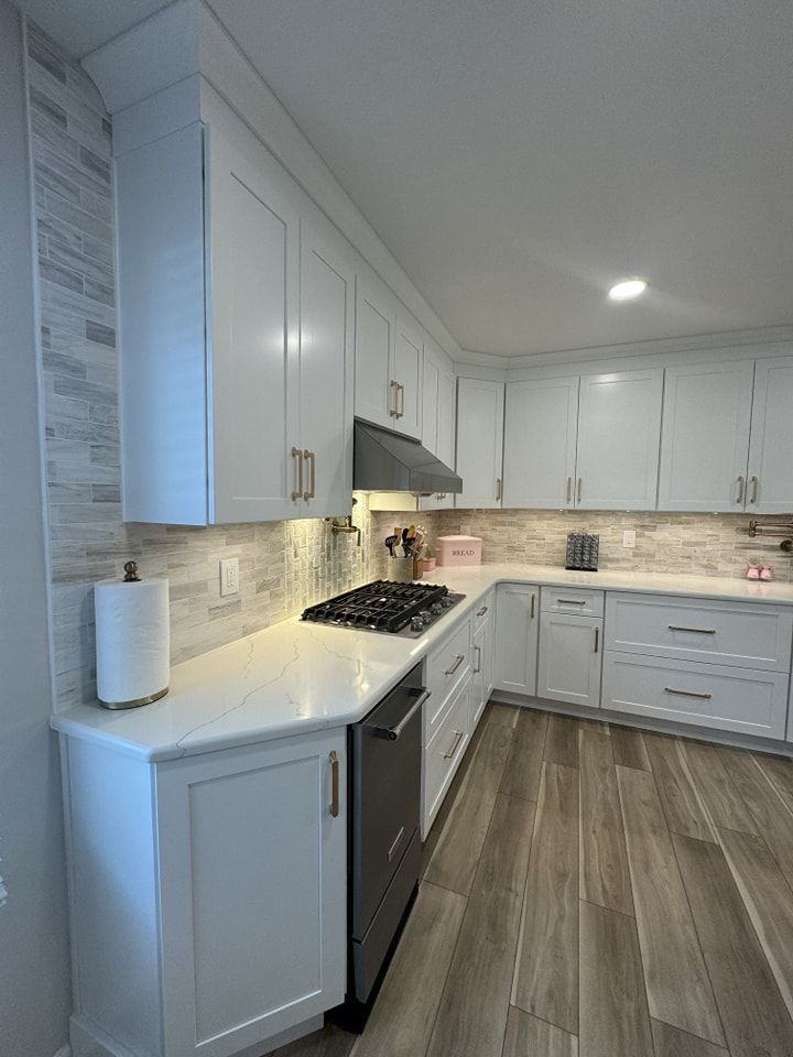 White kitchen with light-colored cabinets, countertops, and backsplash. Stainless steel appliances and wood-look flooring.