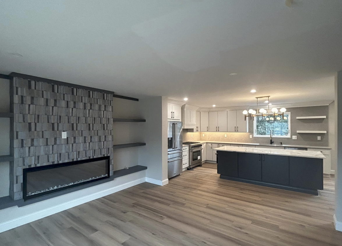 Open-concept living space with a kitchen and fireplace. Gray and white color scheme, wood floors.